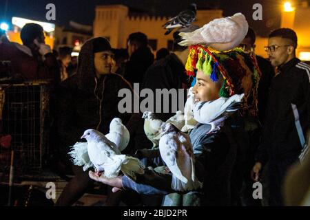 Mädchen mit Tauben bedeckt auf Jemaa el-Fnaa Markt in der Nacht, Marrakesch, Marokko Stockfoto