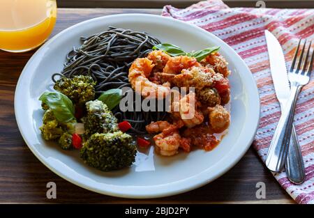 Schwarze Spaghetti mit Garnelentomatensauce und gebackenem Brokkoli mit Roquefort-Käse. Orangensaft Stockfoto