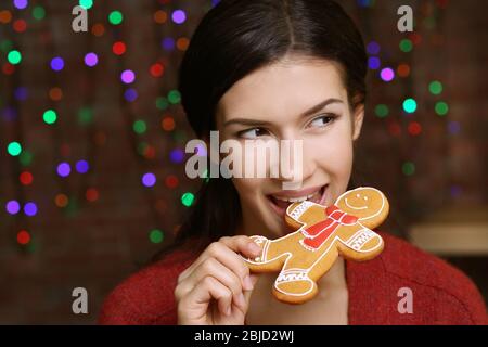Hübsche junge Frau mit leckeren Weihnachts-Cookie gegen defokussed Lichter, Nahaufnahme Stockfoto