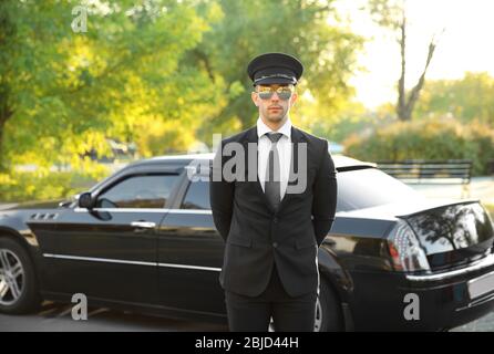 Junger Chauffeur steht in der Nähe von Luxuswagen auf der Straße Stockfoto