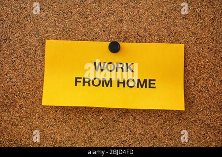 Arbeit von zu Hause auf einem gelben Stück Papier geschrieben, das auf einem Pinnwand ist. Remote Work Konzept. Nahaufnahme. Stockfoto