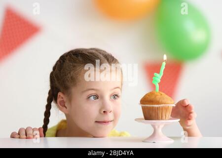 Nettes kleines Mädchen in der Nähe Tisch mit Geburtstagskuchen zu Hause Stockfoto