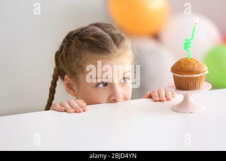 Nettes kleines Mädchen in der Nähe Tisch mit Geburtstagskuchen zu Hause Stockfoto