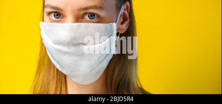 Porträt einer Frau in einer Gaze-Maske auf gelbem Hintergrund mit Kopierraum, der auf die Kamera schaut. Coronavirus-Konzept. Stockfoto