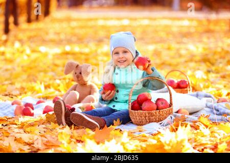 Nettes kleines Mädchen mit Korb voller roter Äpfel im Herbst Park Stockfoto