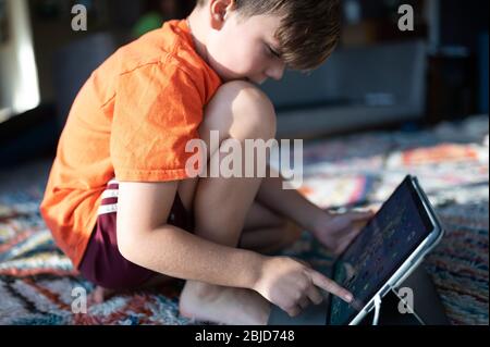 Junge kniend auf Teppich zu Hause mit ipad Tablet Auswahl Anw Stockfoto