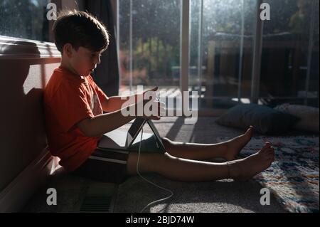 Boy mit ipad Tablet auf dem Boden seines Hauses Mit Sonne im Fenster Stockfoto