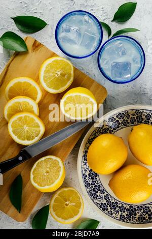 Frisch geschnittene Zitronen mit Gläsern Zitronensaft und Eis auf einem weißen Tisch mit gefallenen Blättern bei einem Picknick im Freien. Erfrischende, gesunde, vitaminreiche fru Stockfoto