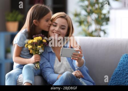 Schöne junge Frau und ihre Tochter machen Selfie während sie zu Hause auf dem Sofa sitzen. Muttertag Konzept Stockfoto