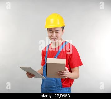 Asiatische Lagerarbeiter mit Tablet-Computer und Karton, auf hellem Hintergrund Stockfoto