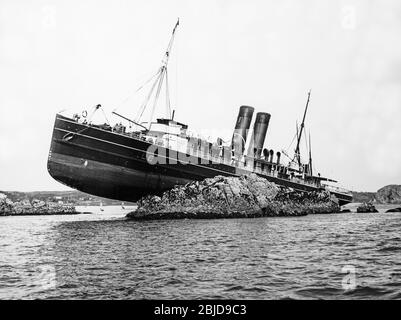 Vintage frühen zwanzigsten Jahrhunderts schwarz-weiß-Foto zeigt ein Dampf-Kreuzfahrt-Schiff, das auf einigen Felsen auf Grund gelaufen ist. Das Schiff hat zwei Trichter, hat aber keinen Namen. Stockfoto