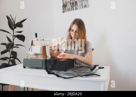 Das Mädchen Nähkleid aus schwarzem Stoff Tüll auf einer Vintage-Nähmaschine im Raum Arbeitsplatz handgemachte Hobby Stockfoto