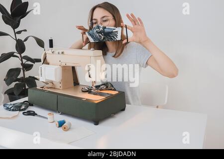 Mädchen Nähen schützende Medizin Maske auf Nähmaschine zu Hause, um die Grippe zu verhindern. Covid-19 im Raum mit weißem Hintergrund Home Workplace Stockfoto