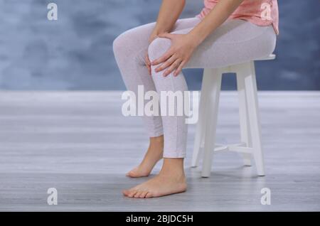 Junge Frau, die an Knieschmerzen leidet, während sie im Haus auf dem Hocker sitzt Stockfoto