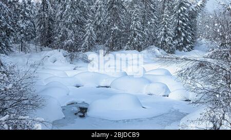 Schneebälle auf einem eisigen Fluss mit Schneeflocken und Bäumen Stockfoto
