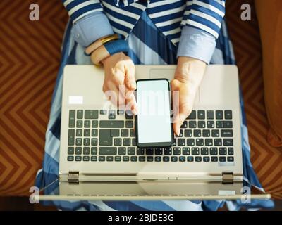 Obere Ansicht der Frau mit Laptop mit Smartphone mit leerem Bildschirm zu Hause in sonnigen Tag. Stockfoto