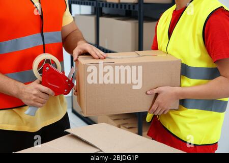 Nahaufnahme von Arbeitern, die Pakete mit Klebeband im Lager verpacken Stockfoto