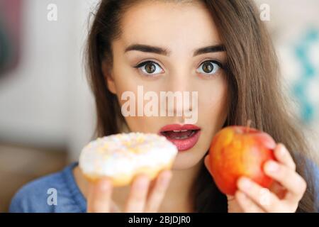 Schöne junge Frau, die Wahl zwischen Apple und Krapfen, Nahaufnahme Stockfoto