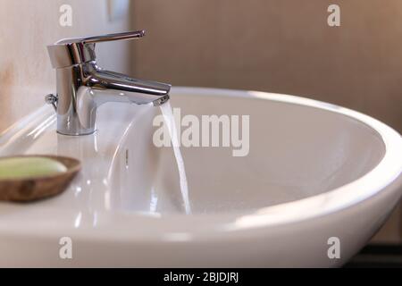 Fließendes Wasser aus dem Wasserhahn wird in das Waschbecken geschüttet. Konzepte der Reinigung, Hygiene, Geldverschwendung, Einsparung von Geld bei Versorgungsunternehmen, sparsamer Umgang mit Wasser Stockfoto