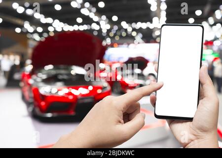 Mockup Bild der Hand hält leere Bildschirm Handy und zeigt auf Smartphone mit verschwommenem Hintergrund der neuen Autos im Showroom anzeigen, Kauf neues Auto. Stockfoto