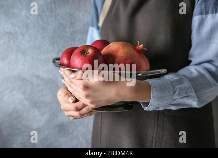 Frau in Schürze hält Sieb mit Äpfeln und Granatapfel, Nahaufnahme Stockfoto
