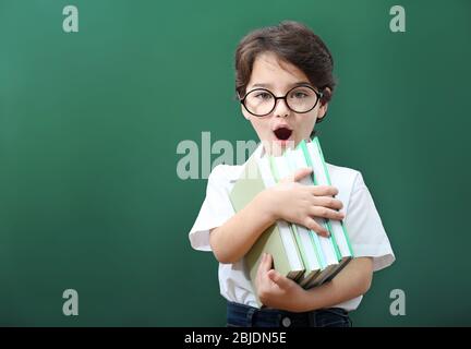 Niedlicher kleiner Junge in einer Brille mit Büchern auf grünem Hintergrund Stockfoto