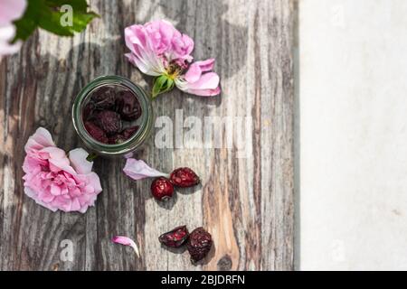 Getrocknete Beeren von Hündin oder Hagebutte mit frischen Rosen und Blättern auf Holztisch.Draufsicht.Selektiver Fokus Platz für Text Stockfoto