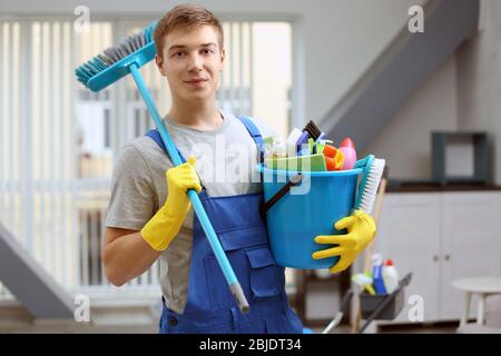 Junger Mann hält Eimer mit Reinigungsgeräten und Zubehör im Haus Stockfoto