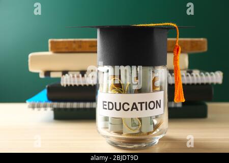 Glas mit Geld für die Bildung auf Holztisch vor grünem Hintergrund Stockfoto