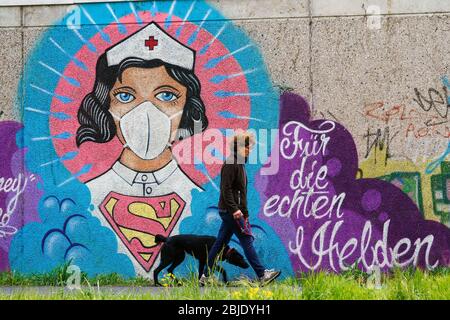 Hamm, 29. April 2020: Poeple passiert ein Coronavirus Graffiti des Straßenkünstlers Kai „Uzey“ Wohlgemuth, das 'Super-Nurse' mit Schutzmaske an einer Wand in Hamm zeigt. Die Schrift sagt: 'Für die wahren Helden' --- Hamm, 29.4.2020 - Corona-Kunst. Das Graffiti „Super-Nurse“ an einer Wand in Hamm. Eine Krankenschwester mit Mundschutz und Supermann-Logo hat der Graffiti-Künstler Kai „Uzey“ Wohlgemuth aus Hamm den echten Helden in der Corona-Krise geweimet. Stockfoto