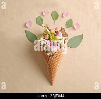 Waffelkegel mit Komposition von schönen Blumen auf hellem Hintergrund Stockfoto