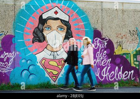 Hamm, 29. April 2020: Poeple passiert ein Coronavirus Graffiti des Straßenkünstlers Kai „Uzey“ Wohlgemuth, das 'Super-Nurse' mit Schutzmaske an einer Wand in Hamm zeigt. Die Schrift sagt: 'Für die wahren Helden' --- Hamm, 29.4.2020 - Corona-Kunst. Das Graffiti „Super-Nurse“ an einer Wand in Hamm. Eine Krankenschwester mit Mundschutz und Supermann-Logo hat der Graffiti-Künstler Kai „Uzey“ Wohlgemuth aus Hamm den echten Helden in der Corona-Krise geweimet. Stockfoto