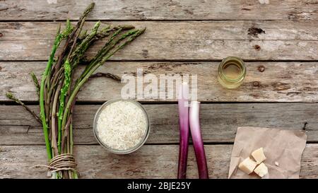 Zutaten für italienisches Risotto auf Holztisch: Reis, Wildspargel, Parmesan, grüne Zwiebeln, Schalotten oder Schalotten. Draufsicht, Platz für Text Stockfoto