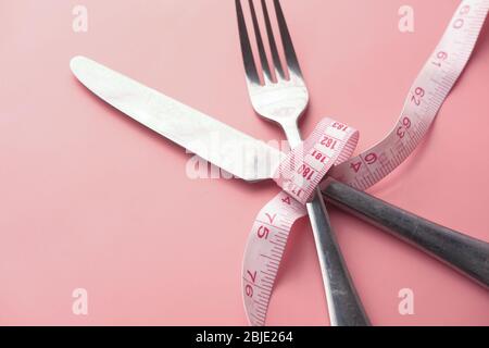 Messer und Gabel in Maßband auf rosa Hintergrund gewickelt. Stockfoto