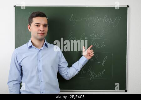 Hübscher junger Lehrer erklärt mathematische Formeln auf der Tafel Stockfoto