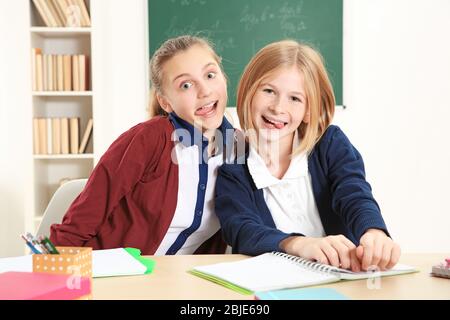 Zwei süße Mädchen sitzen am Schreibtisch in der Schulklasse Stockfoto