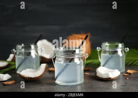 Drei Maurerkrüge mit Kokoswasser und frischen Nüssen auf dunklem Hintergrund Stockfoto