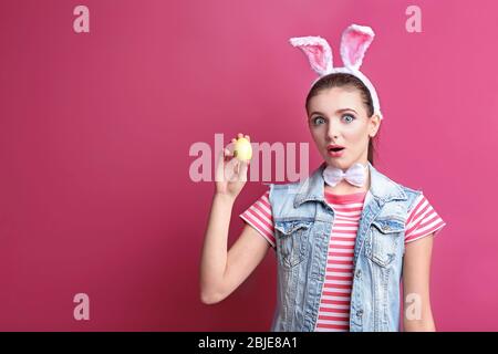 Schönes Mädchen mit Hasenohren und Osterei auf farbigen Hintergrund Stockfoto