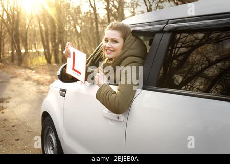 Junge Frau mit Fahrerschild des Lernenden beim Blick aus dem Autofenster Stockfoto