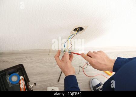 Elektriker, der die Kabel an die Steckdose im neuen Gebäude ansteckt Stockfoto