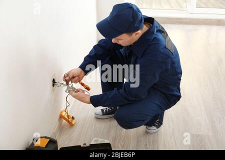 Elektriker, der die Kabel an die Steckdose im neuen Gebäude ansteckt Stockfoto