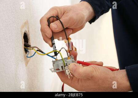 Elektriker, der Kabel an der Steckdose im neuen Gebäude ansteckt, Nahaufnahme Stockfoto