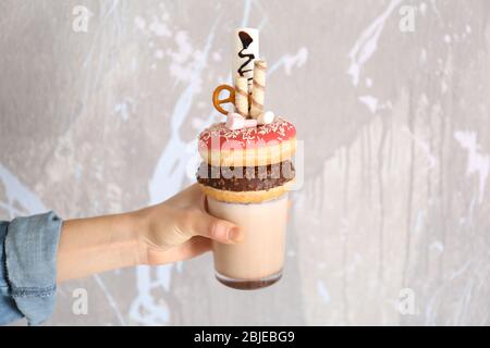 Hand hält Milchshake, Donuts und andere Süßigkeiten in Glas auf farbigen Hintergrund Stockfoto