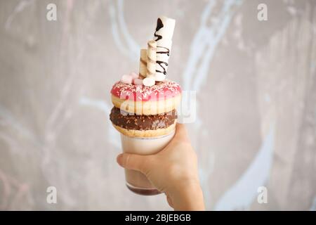 Hand hält Milchshake, Donuts und andere Süßigkeiten in Glas auf farbigen Hintergrund Stockfoto