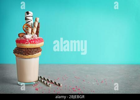 Milchshake, Donuts und andere Süßigkeiten in Glas auf farbigem Hintergrund Stockfoto