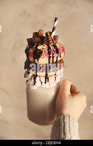 Hand hält Milchshake, Donuts und andere Süßigkeiten in Glas auf farbigen Hintergrund Stockfoto