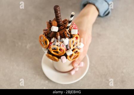 Hand hält Milchshake, Donuts und andere Süßigkeiten in Glas auf farbigen Hintergrund Stockfoto