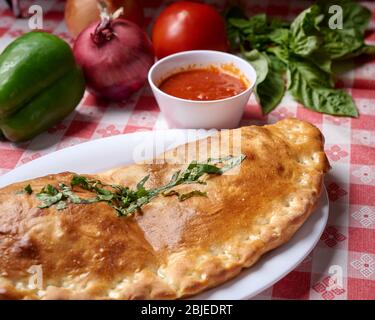 Frisch gebackener Stromboli auf weißem Teller mit frischen Zutaten Stockfoto