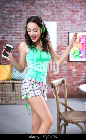 Glückliche junge Frau in Kopfhörer Musik hören und tanzen zu Hause Stockfoto