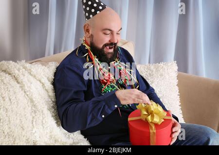 Lustige fette Mann mit Geburtstagsgeschenk sitzen auf dem Sofa zu Hause Stockfoto